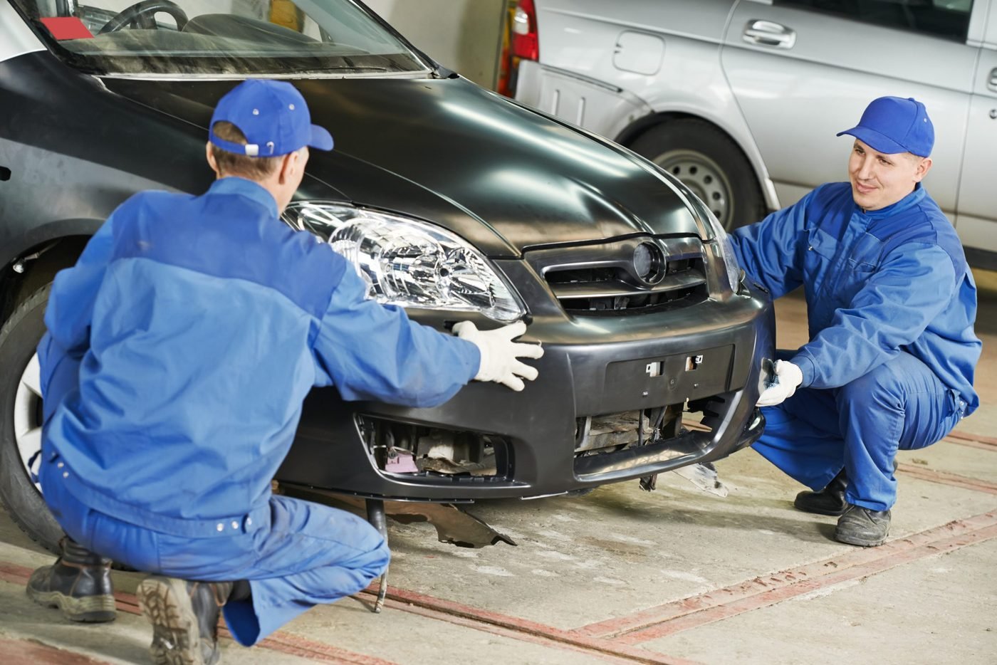 Auto repair technicians fitting a car bumper in a workshop