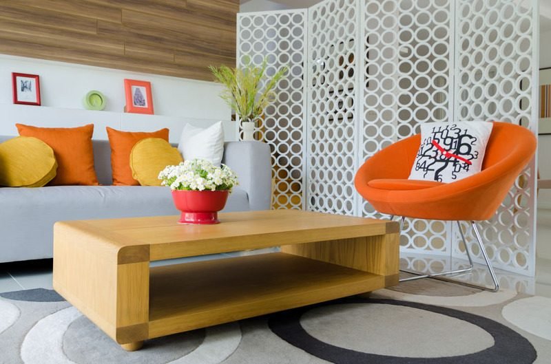 A bright living room with an orange chair and wooden table
