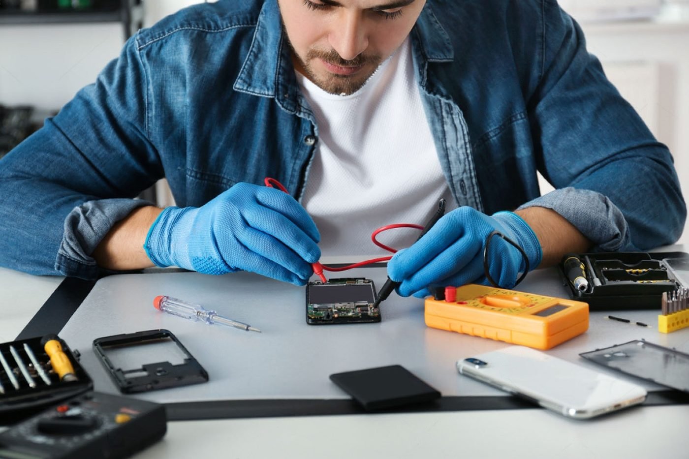 A technician repairing a mobile phone with a multimeter